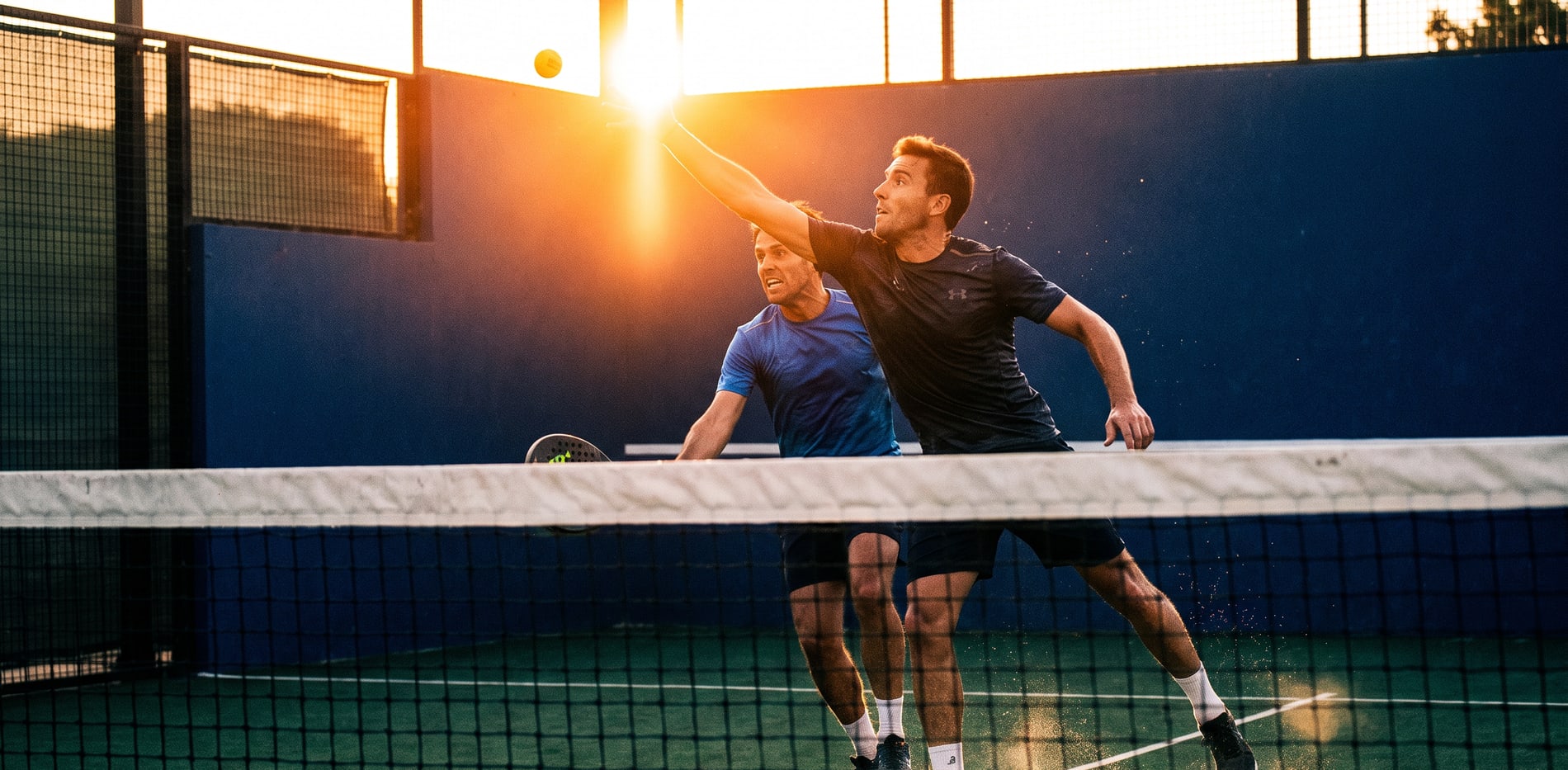 Dos jugadores de pádel en un remate al atardecer sobre la pista de pádel